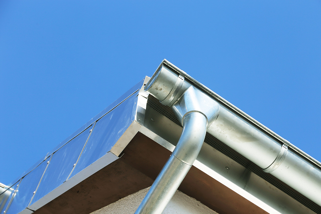 Metall-Dachrinne und Fallrohr an der Ecke eines Hauses vor klarem blauem Himmel
