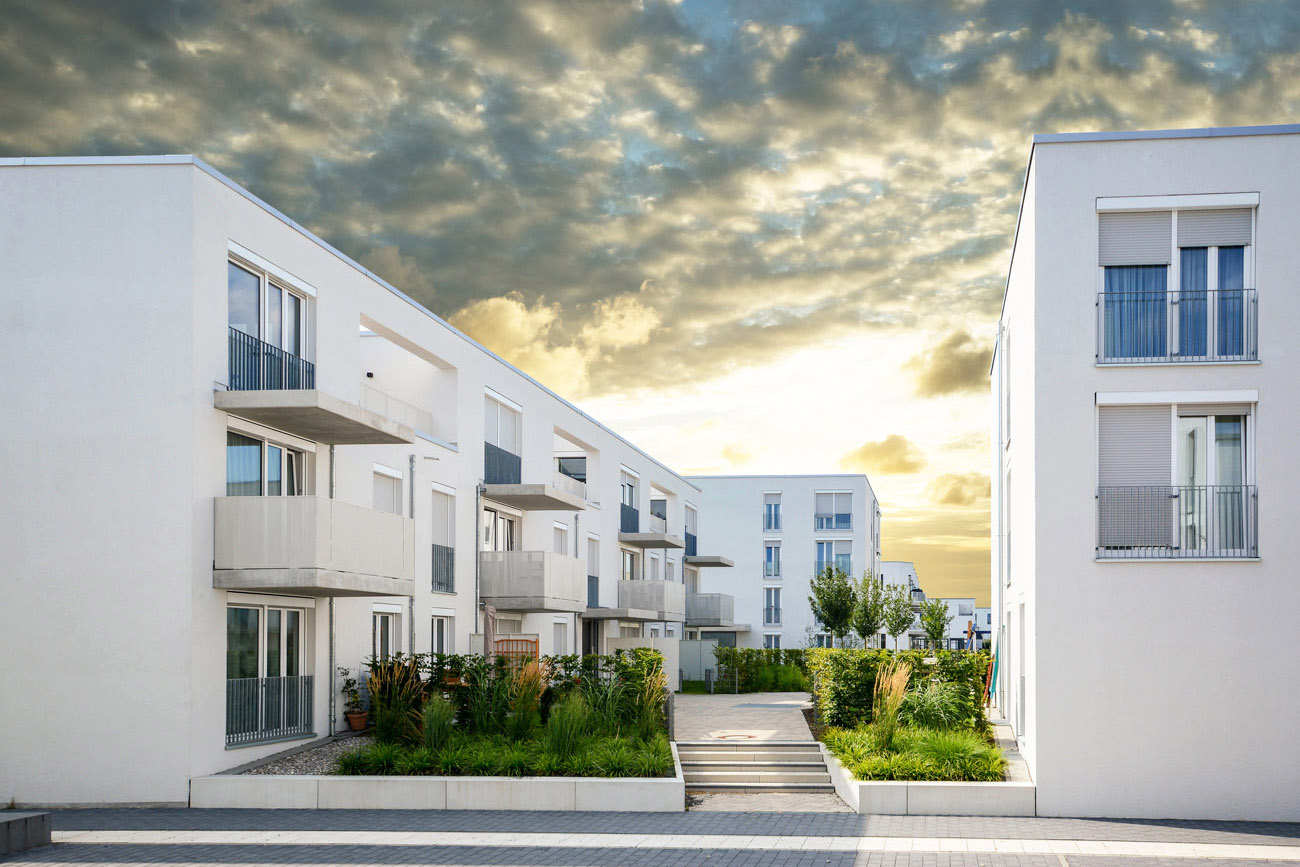 Moderne weiße Wohngebäude mit Balkonen und begrünten Innenhof bei bewölktem Himmel
