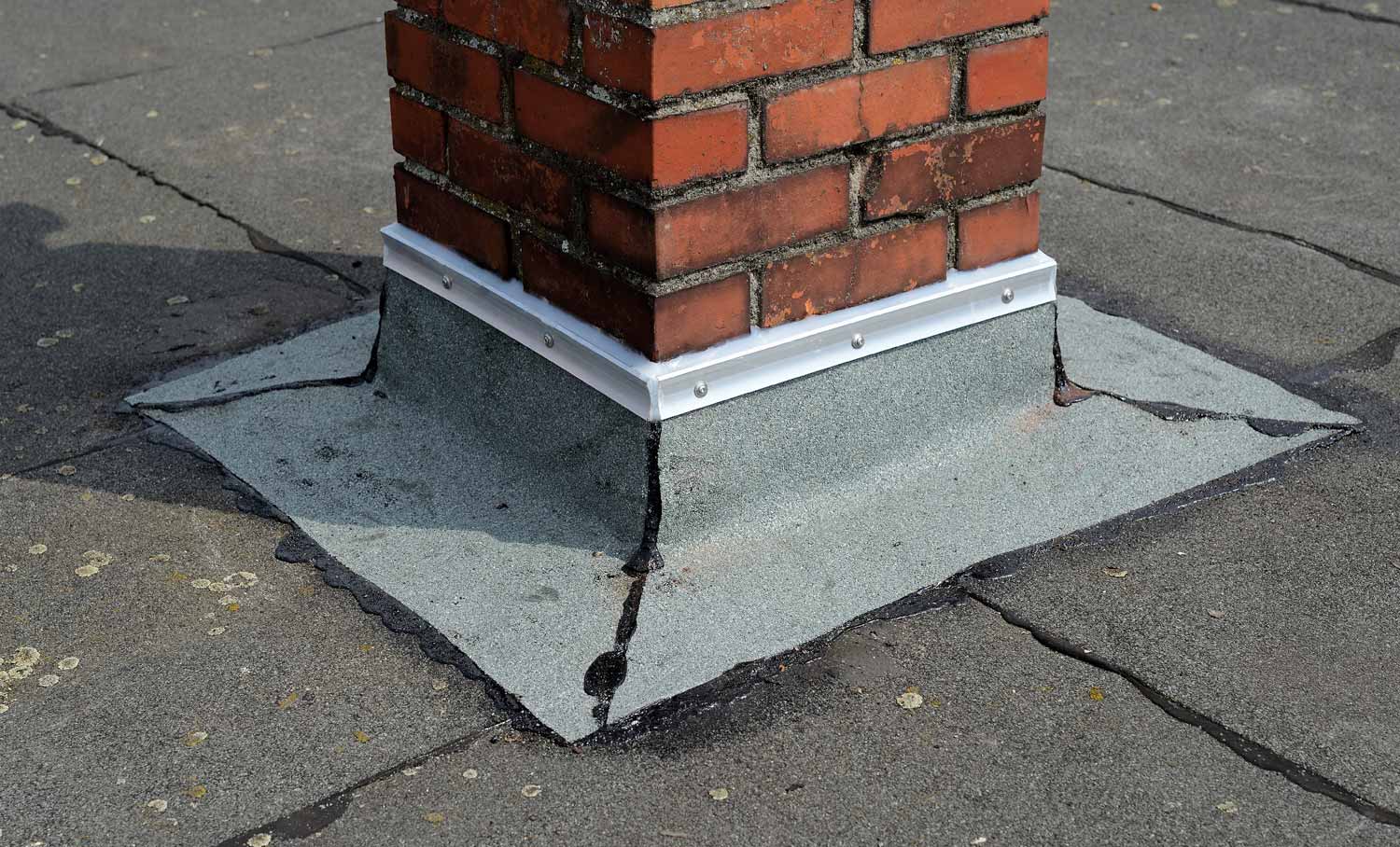 Abdichtung aus Bitumenbahnen und Metallmanschette an einem gemauerten Schornstein auf Flachdach